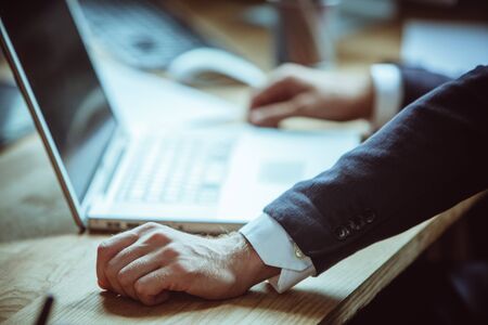 Well-dressed businessman uses laptop computer while working at workplace in office. Highlighted focus on male hand in foreground. Close up. Tinted image.の写真素材