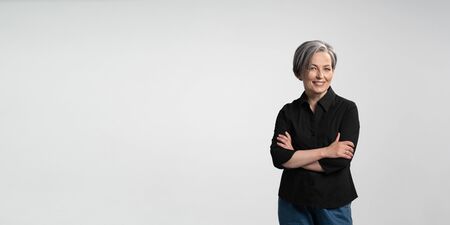 Confident mature woman smiling arms crossed. Gray haired businesswoman in black shirt on white...