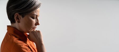 Sad or depressed mature woman thoughtfully touches her chin with hand. Profile view. Copy spase for...