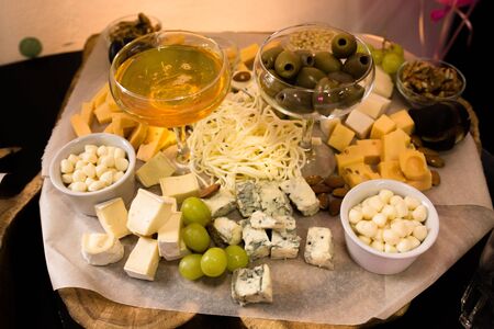 Assorted of cheese with honey, grapes and green olives on cheeseboard or wooden plank. Delicatessen or tasty appetizers concept.の写真素材