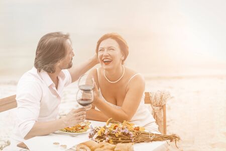 Happy mature man and woman laughs drinking wine outdoors. Couple in love resting together in coast cafe. Tinted image.の写真素材