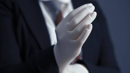 Business person puts on white disposable gloves. Business during and after quarantine. Close up shot.の写真素材