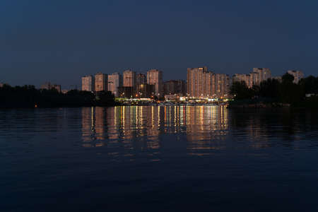 Evening at Dnipro River. Golden lights of modern buildings reflect in water. View on Poznyaki district at left side of Dnieper. August, 2019. Kiev, Ukraine.のeditorial素材