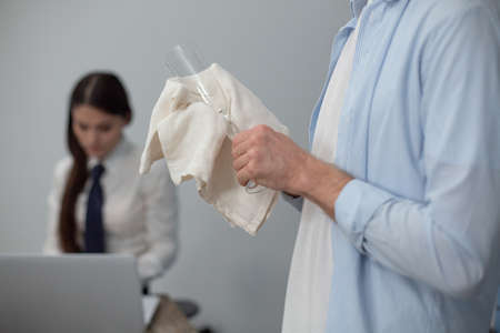 Man cleaning champagne glass. Mans hands holding empty clear champagne glass and white napkin for cleaning. Close up shot. Woman on blurred background.の写真素材