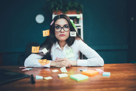 Crazy woman with reminder labels sitting at office desk. Many memory stickers pasted on young...