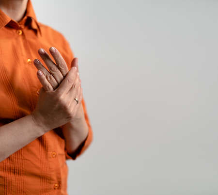 Mature Caucasian woman in orange shirts cares for hands skin. Female hands, close up shot. Square template with text space for publication on social networks.の写真素材
