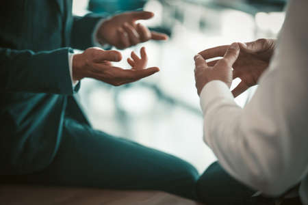 Two business people have conversation sitting on office desk. Close up shot of office workers hands. Tinted image.の写真素材