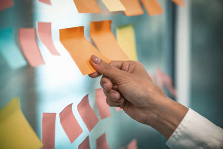 Female hand glues empty sticker on office window. Many colorful note paper stickers with space for...