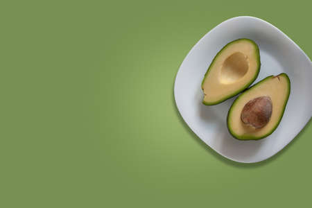 Cut avocado on white plate isolated on light green background. Template or blank for banner with empty space for text. Vegan cuisine concept.の写真素材