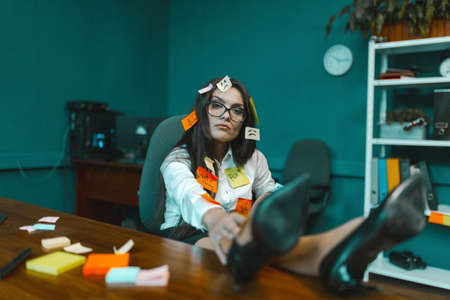 Overworked woman with pasted stickers relaxing in office chair. Young crazy businesswoman with lot...