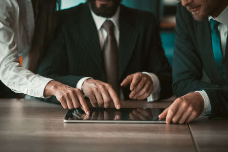 Business coworking. Creative businesspeople touching by fingers digital tablet working on new...