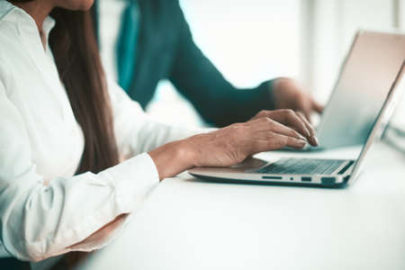 Office workers at a laptop. Employees hands are printed on the keyboard. In the background is a colleague in a suit. High quality photo.の写真素材