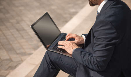 Adult man in business suit sits with laptop on the street. Side view of Caucasian man working on the steps. High quality photo.の写真素材