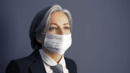 Gray haired businesswoman in protective mask looking at side, Masked fashion Caucasian woman in formal wear isolated on gray background. Epidemic concept.の写真素材