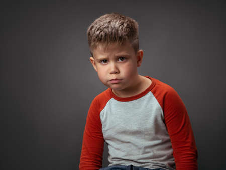 Offended boy looks into the camera. Childrens resentment is a concept. Sad child in the studio on an...