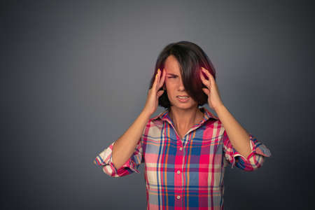 Woman experiences a migraine in studio on an isolated background. Headache concept. Brunette woman holding her head with her hands. Female face expresses pain. High quality photo.の写真素材