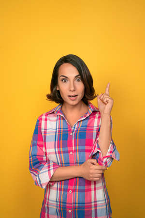 Brunette woman has an idea. Woman lifts her index finger up with an exclamation on her face. High quality photo.の写真素材