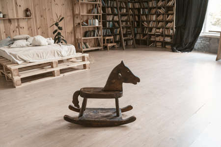 Bedroom in a wooden interior. In the foreground is a wooden horse. In the background is a bed and a bookshelf. High quality photo.の写真素材