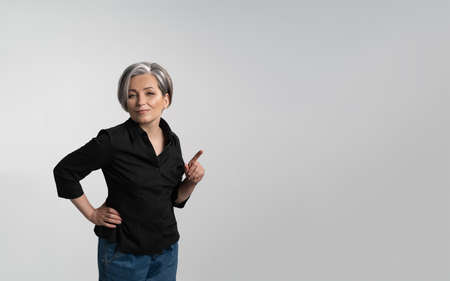 Adult woman in black shirt points her finger at copy space. Template with Grey woman isolated on...