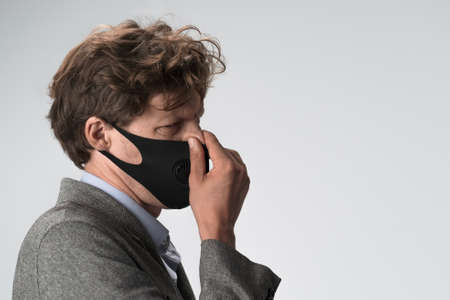 Caucasian man in protective mask winces rubbing his nose. Profile view. Close up shot.