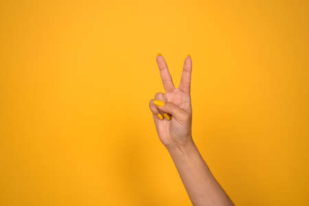 V sign. Female hand shows two fingers or peace gesture. Cut out on yellow background. Copy space.