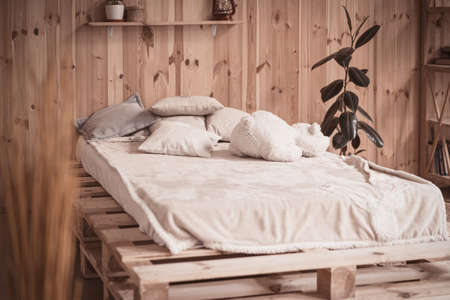Cozy bed with pillows and bear toy in wooden home interior.の写真素材