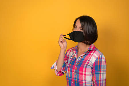 Cute young woman with face protective mask during quarantine. Isolated on yellow background. Virus...