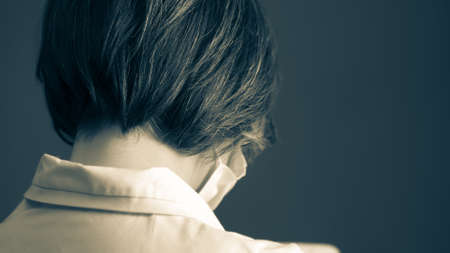 Gray haired female doctor wearing mask and white coat. Close up shot. Rear view. Toned black and white image.の写真素材