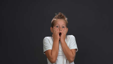 Teen boy expresses omg or shock emotions opened mouth and putting palms to his cheeks. Sale concept. Isolated on gray background. Copy space.の写真素材