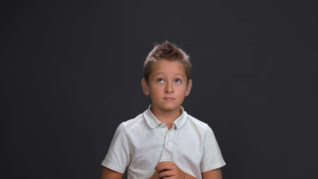 Thoughtful or waiting boy folded his palms looking up. Pensive teenager isolated on gray background. Copy space.の写真素材