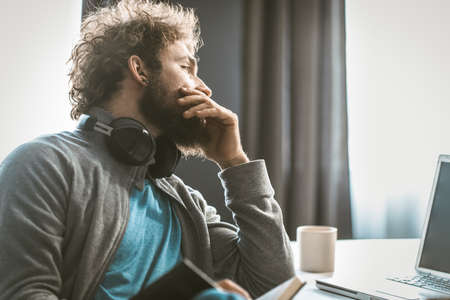 A young entrepreneur brings down accounting. The man takes notes in a notepad and looks at the computer screen sitting at his desk. High quality photoの写真素材