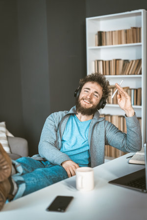 Happy student at home. Remote learning concept. Young man with headphones smiles sitting in front of a computer. High quality photoの写真素材