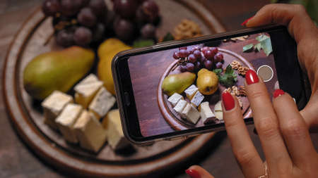 Girl food stylist use her smartphone to take a photos for her cooking blog. Talented food stylist and photographer making preparations for commercial photoshoot.の写真素材
