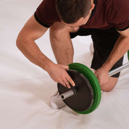 Adding weight to a barbell young man bow on a knee changing black and green plates, equipment for weight training concept. Sports equipment for training. square cropped.の写真素材