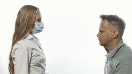 Medic looking at male patient who came for tests wearing a medical face mask. Sad man looking at her with sad eyes. Isolated on white background. Tinted image.の写真素材