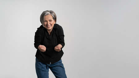Happy to see her grand kids bowed and hands stretched forward grey haired mature woman wearing black shirt isolated on grey background. Human emotions, facial expression concept.の写真素材