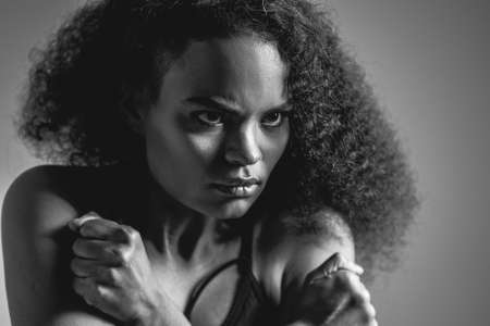 Black and white image. Self-defense, fearful African American girl standing covered with hands in black bare shoulder top isolated on grey background. Human emotions, facial expression concept.の写真素材