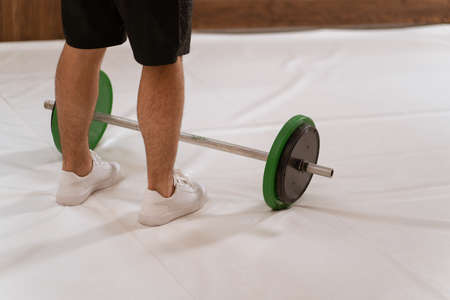 Weightlifting young man taking a brake standing near black and green weight set, equipment for...