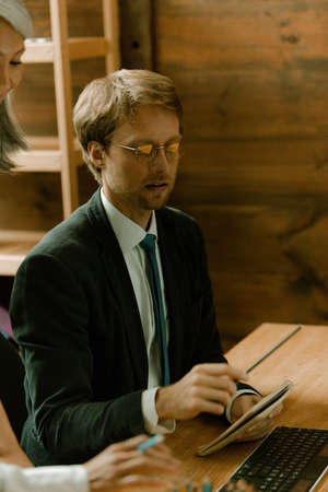Young man with glasses freelancer working on computer in office. Caucasian man showing notes to a...