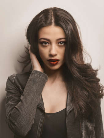 Young woman in black leather with denim jacket with beautiful long dark hair isolated on gray...