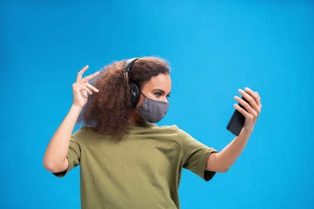 Young African American female listen music on her smartphone wearing headphones in olive t-shirt in...