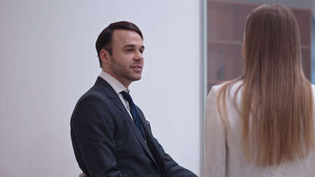 Handsome young businessman talking with female colleague sitting in meeting room behind the glass...