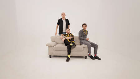 Switching places three young handsome men moving around sofa taking the main place and carry away of...