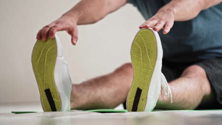 No face visible young fit man doing stretching exercises sitting on the roll mat at home. Amateur...