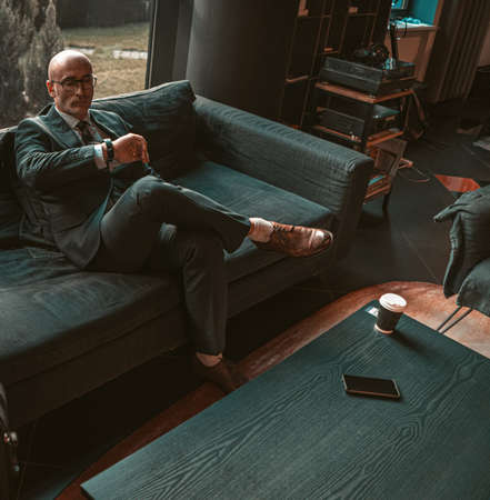 Adult respectable bald businessman looking at watches on his hand waiting for a business meeting in...