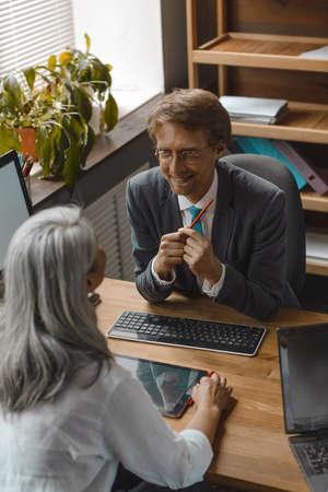 Two supervisors sitting one against another and cheerfully talking together. Multi ethnic business people working on computers sitting at the modern office. Toned image.の写真素材