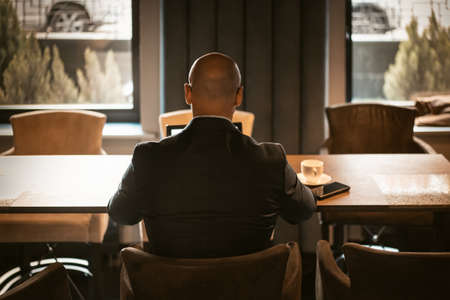Back view of elegant CEO dressed in expensive suit sitting at the table in the modern expensive office interior, bald male working on laptop. Back view.の写真素材