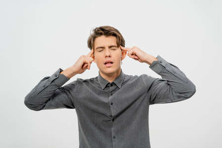 Tired or trying to rethink the information received while experiencing a headache young handsome man in grey shirt, look with cool hairstyle isolated on white background.の写真素材