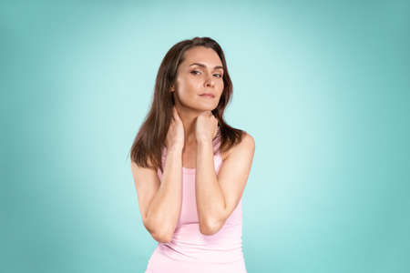 Charming woman with no makeup standing with hands on her neck, massaging it gently attractive...