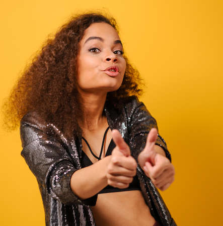 Thumbs up happy Afro American girl with beautiful hairstyle posing smile looking side away with hand...